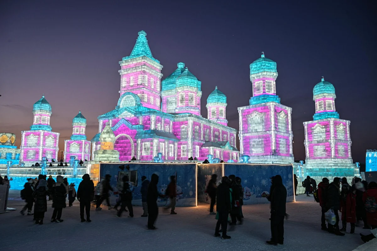 Illuminated ice castle glowing in pink and blue at the Harbin Ice and Snow Festival at night